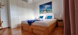 Une chambre à coucher avec un lit en bois, une armoire blanche et un tableau représentant une scène de plage.