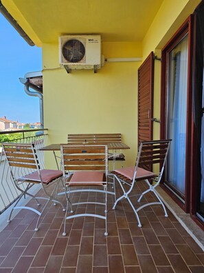 A balcony with a table and chairs, an air conditioning unit, and a sliding glass door. - Vacation apartment with garden and barbecue facilities - Apartman 3 (Valbandon)