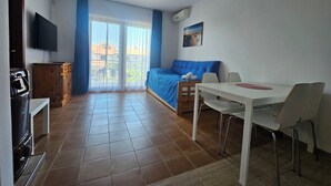Ein Schlafzimmer mit Bett, Fernseher, Esstisch mit Stühlen und Blick ins Freie.