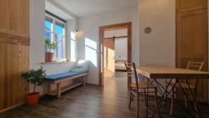 Et værelse med en træbænk ved et vindue, et spisebord med stole og en dør til et andet rum.