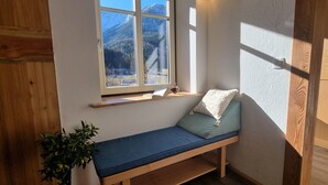 En hyggelig læsekrog med en bænk, et lille bord og et vindue med udsigt over et bjerglandskab.