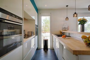 A modern kitchen with stainless steel appliances, a wooden countertop, and pendant lighting. - Les Embruns d'Arcachon - Villa with heated pool (Arcachon)