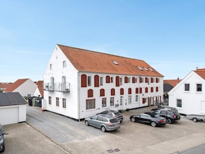 A white building with a red-tiled roof, multiple windows, and a parking area with cars. - 4 Star Holiday Home in Lokken (Lokken)