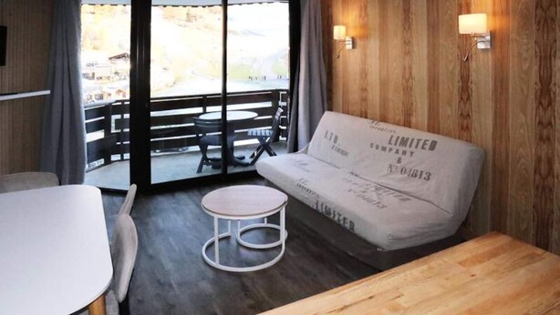 A room with a wooden wall, a white sofa, a round table, and a view through a glass door. - Apartment in Les Carlines by Ski Slopes (Les Orres)