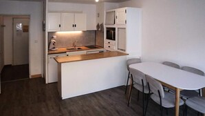 A compact kitchen with a central island, a dining table with chairs, and a built-in oven. - Apartment in Les Carlines by Ski Slopes (Les Orres)