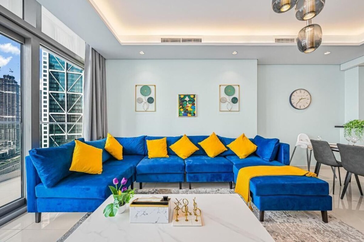 Ein modernes Wohnzimmer mit einem blauen Modulsofa, einem weißen Couchtisch und einem Essbereich mit einem grauen Sessel und einem kleinen Tisch.