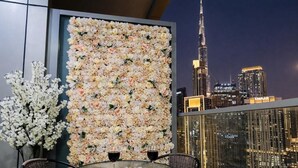 A balcony with a floral wall, a table with wine glasses, and a view of the Burj Khalifa at night. - Lucky Getaways (Dubai)