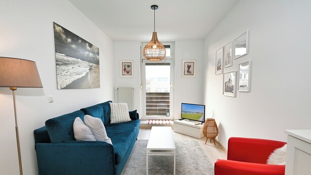 Een moderne woonkamer met een blauwe bank, een rode fauteuil, een witte salontafel en een televisie.