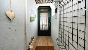 Een smalle gang met een houten vloer, een bruin vloerkleed, een groene deur met een witte gordijn en een hartvormige decoratie aan de muur.