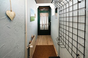 Ein schmaler Korridor mit Holzboden, einem braunen Teppich, einer grünen Tür mit weißem Vorhang und einer herzförmigen Dekoration an der Wand.