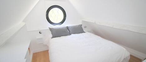 Een kleine, witte eenpersoonskamer met dakraam en houten vloer.