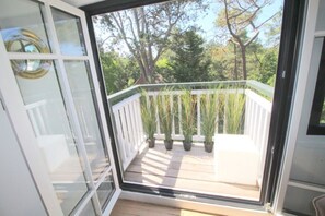 Varanda com guarda branco, plantas em vasos e vista para árvores.