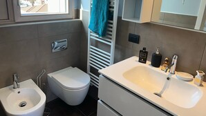 Un baño moderno con bidé, inodoro, lavamanos y perchero para toallas.