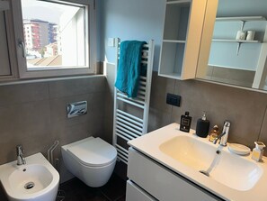 A modern bathroom with a bidet, toilet, sink, and towel rack. - Penthouse Don Minzoni in Verbania with terrace (Verbania)