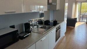Una cocina moderna con armarios blancos, un lavamanos de acero inoxidable, una cafetera negra y un hervidor eléctrico negro.
