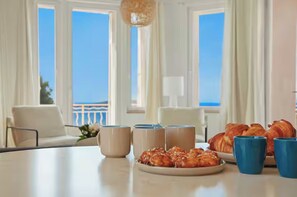 A dining table with pastries and coffee cups, a sofa, and a view of the sea through large windows. - Exceptional sea-facing duplex (Hyères)