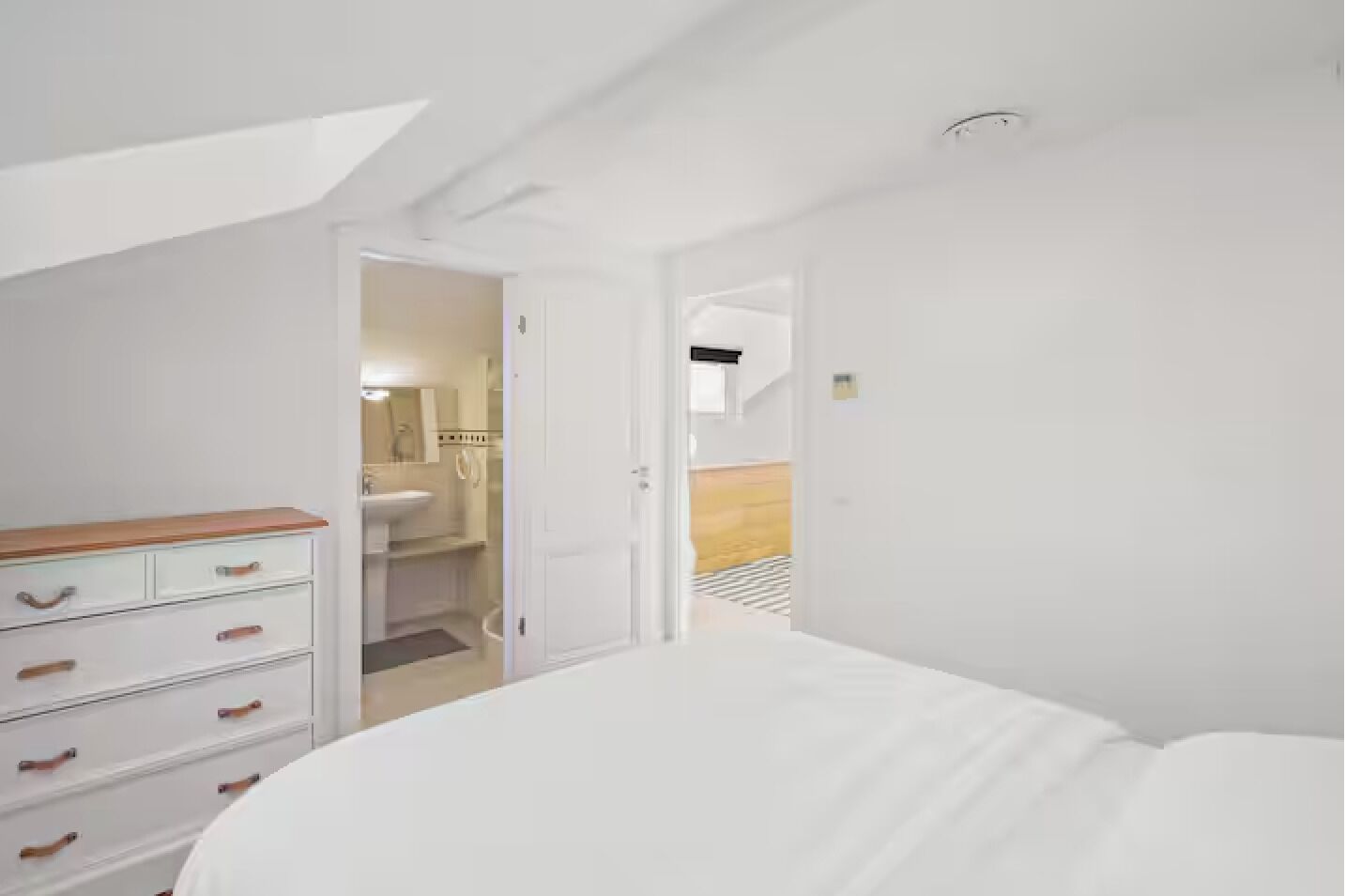A bedroom with a white bed, a wooden dresser, and a walk-in closet.