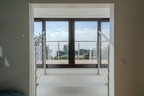 Ein modernes Interieur mit einer Treppe, die zu einem Balkon mit Glastüren und Metallgeländern führt.