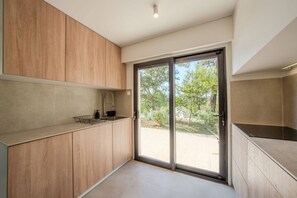 Eine moderne Küche mit Holzausbau, einer Edelstahlspüle und einer Glastür, die zu einem Außenbereich führt.