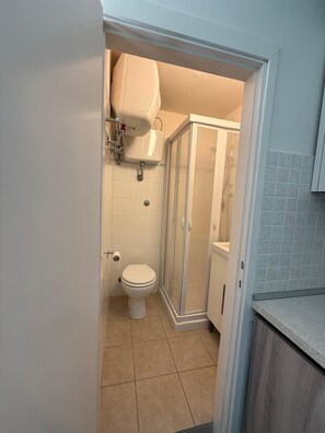 Et badeværelse med toilet, bruseniche og toiletpapirholder.