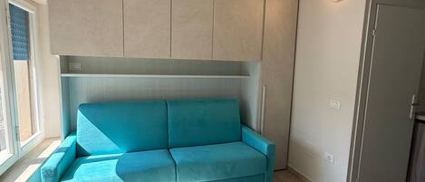 A room with a teal sofa, a window, and a door.