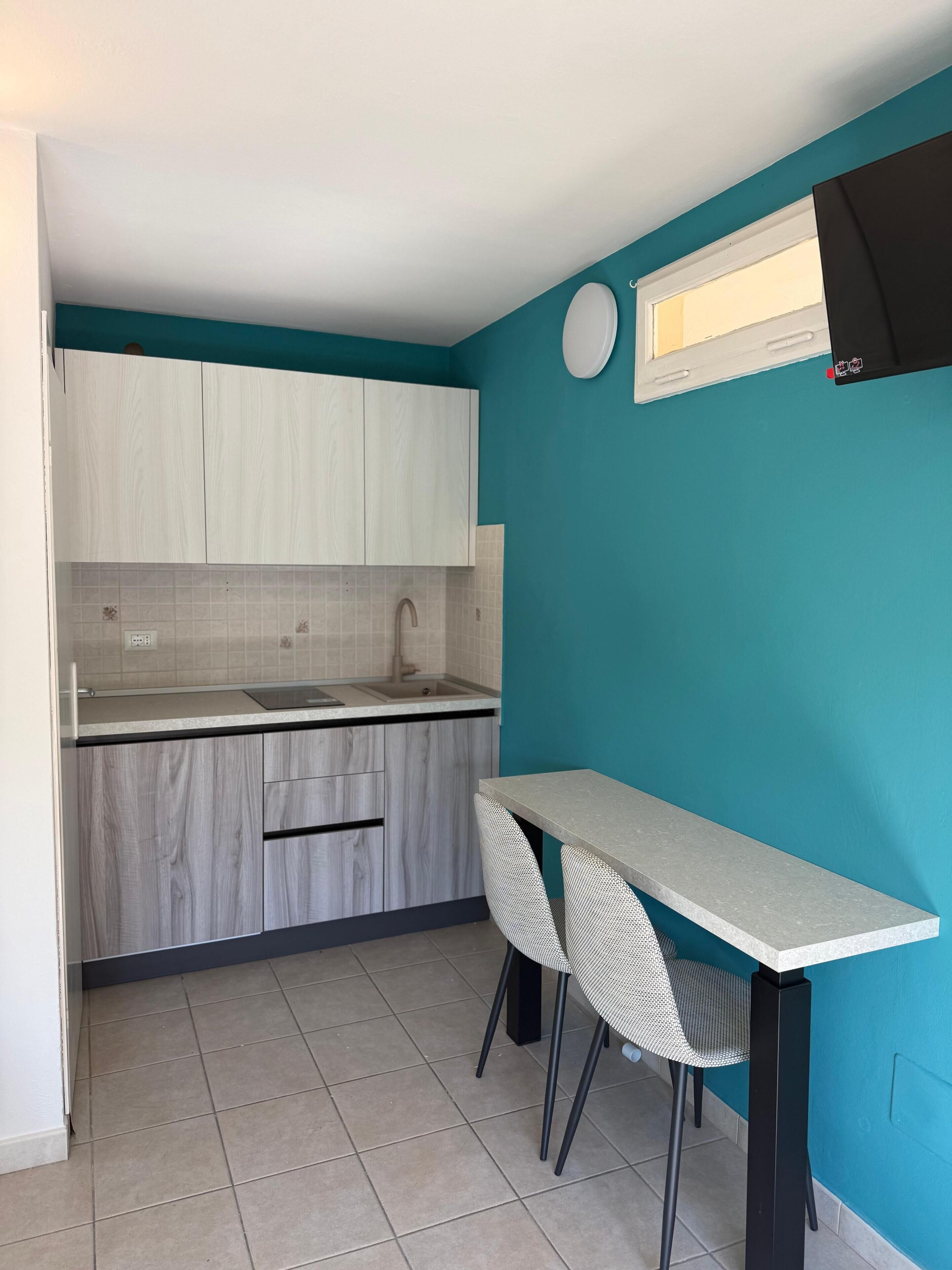 A compact kitchen with a sink, cabinets, and a dining area with chairs.