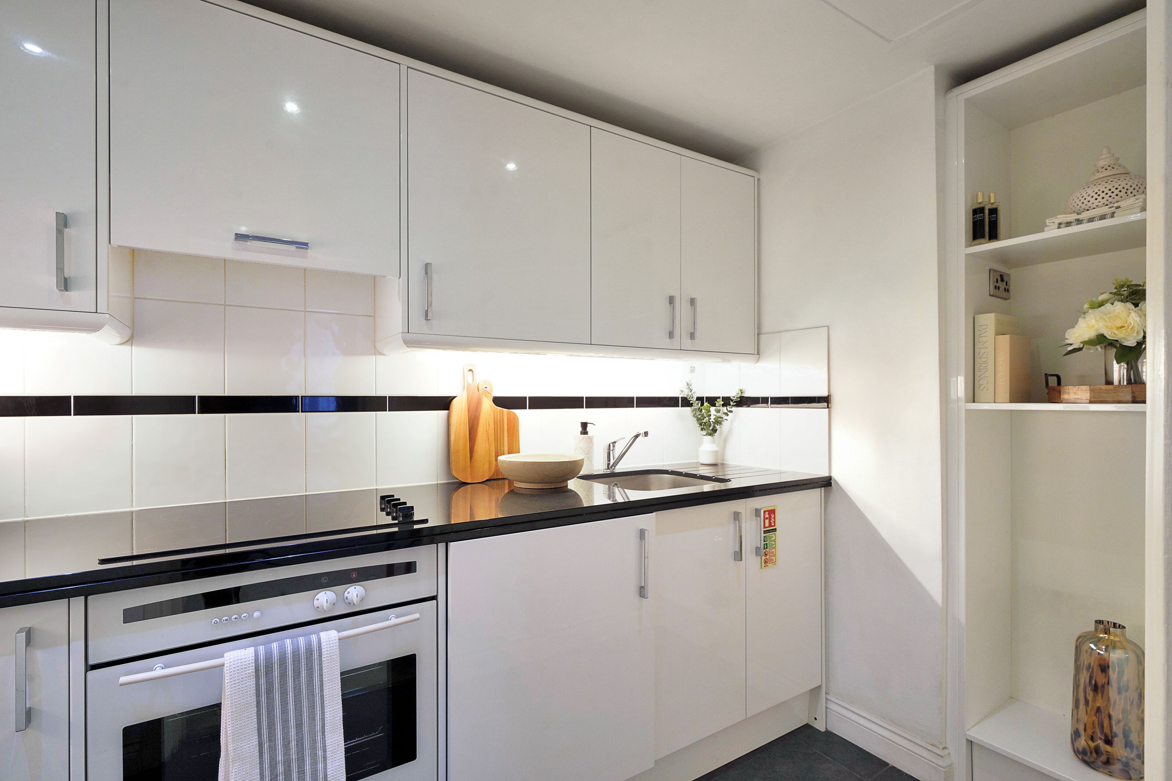 Una cocina moderna con gabinetes blancos, encimera negra y electrodomésticos de acero inoxidable.