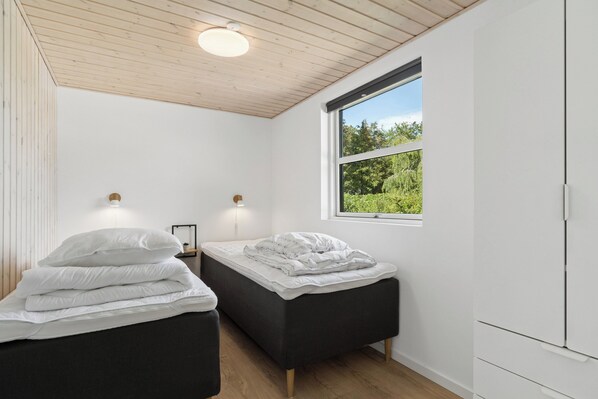 A bedroom with two beds, a window with a view of greenery, and a wooden ceiling.