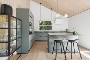 A modern kitchen with a central island, bar stools, and a glass display cabinet.