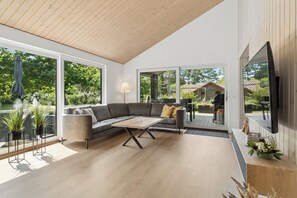 Un salon moderne avec un canapé d’angle, une table basse et de grandes fenêtres donnant sur l’extérieur.