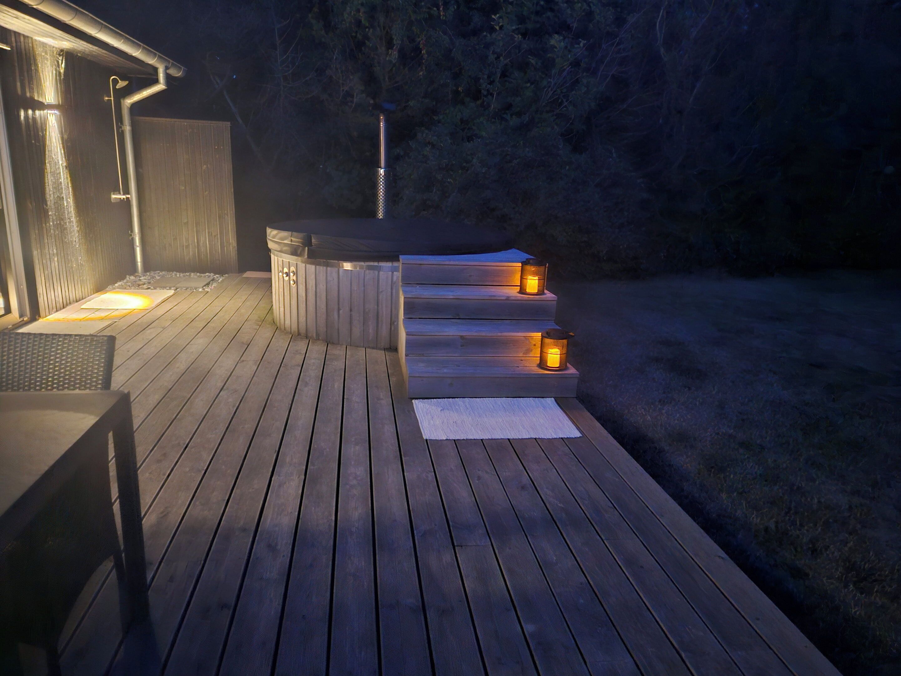 Una terraza de madera con un jacuzzi y escalones que conducen a una zona cubierta.