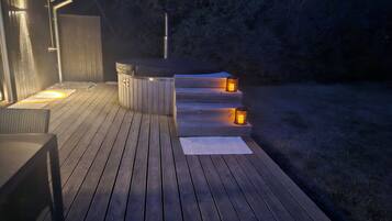 Una terraza de madera con un jacuzzi y escalones que conducen a una zona cubierta.