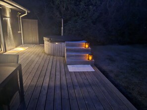 Une terrasse en bois avec un jacuzzi et des marches menant à une zone abritée.