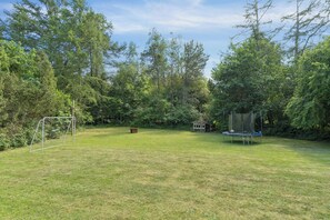 Une cour arrière verdoyante avec un but de football, un trampoline et de nombreux arbres.