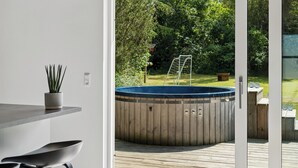 A modern outdoor deck with a hot tub, a wooden fence, and a grassy yard. - New and modern holiday home with hot tub (Grenaa)