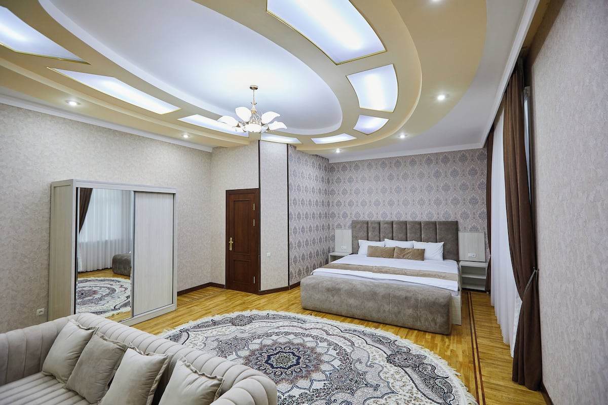 A modern bedroom with a large bed, a sofa, a mirror, and a ceiling with recessed lighting.