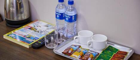 A tray with two white cups, two bottles of water, a kettle, a remote control, a magazine, and several tea packets.