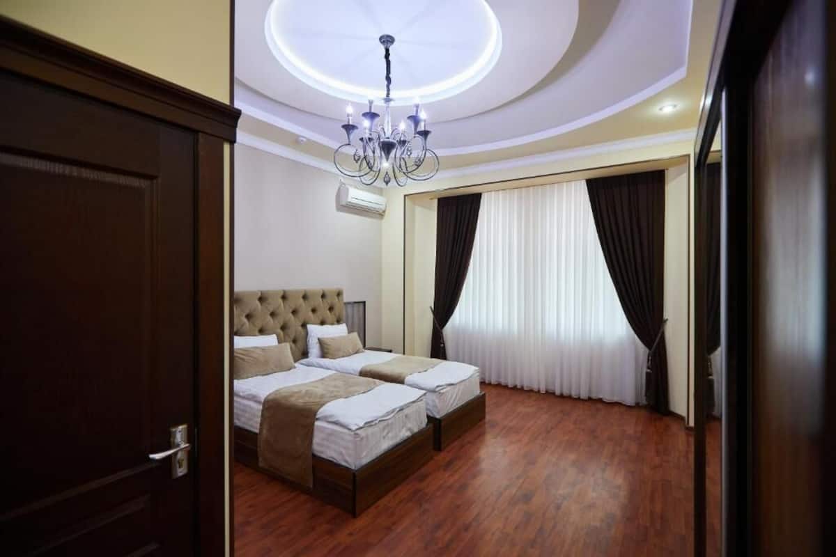 A hotel room with two beds, a chandelier, and a large window with curtains.