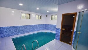 Una piscina con bordo piastrellato blu, una porta con pannello in vetro e una finestra con tenda.