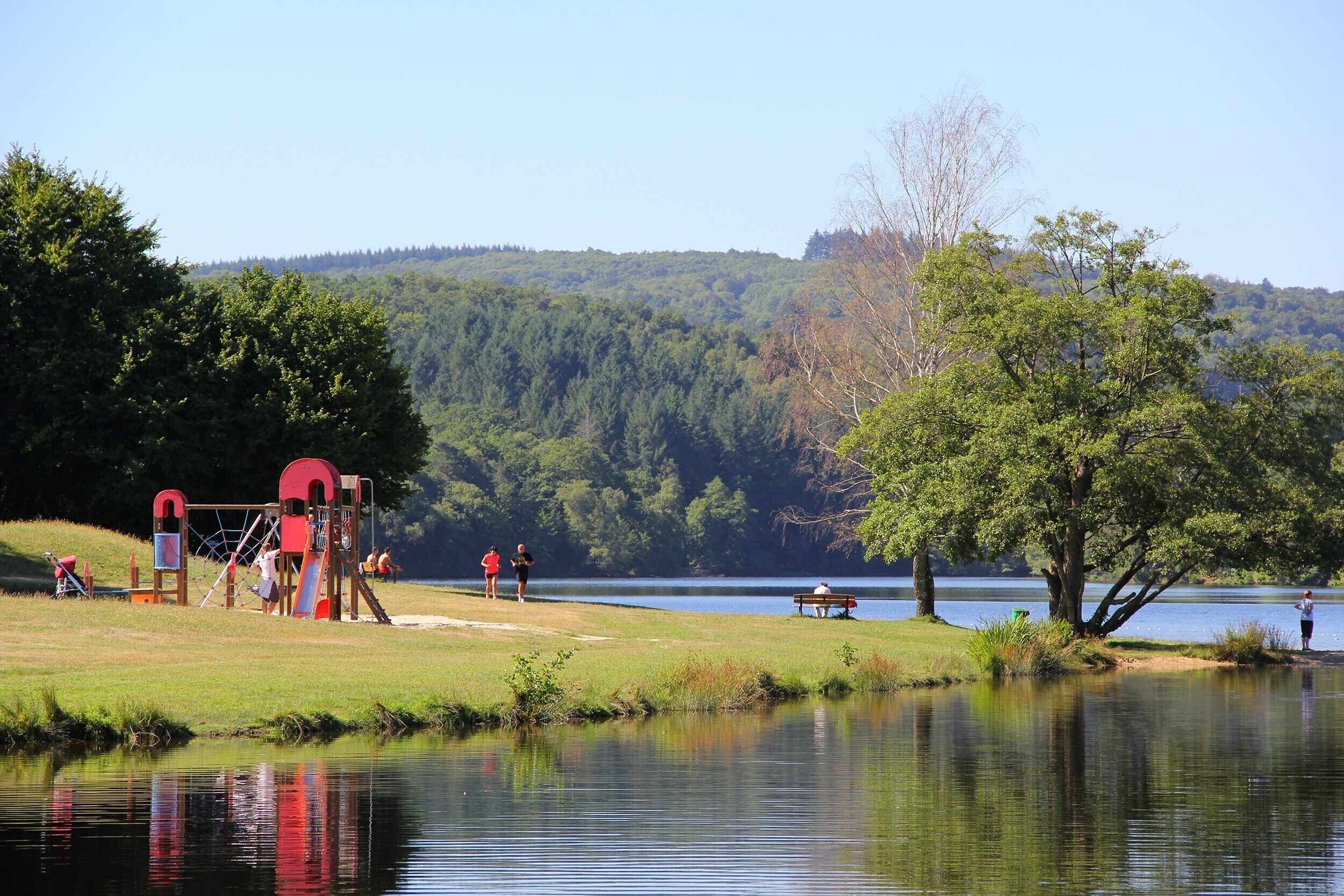 Ein Park am See mit Spielgeräten, einer Bank und einer Person beim Angeln.