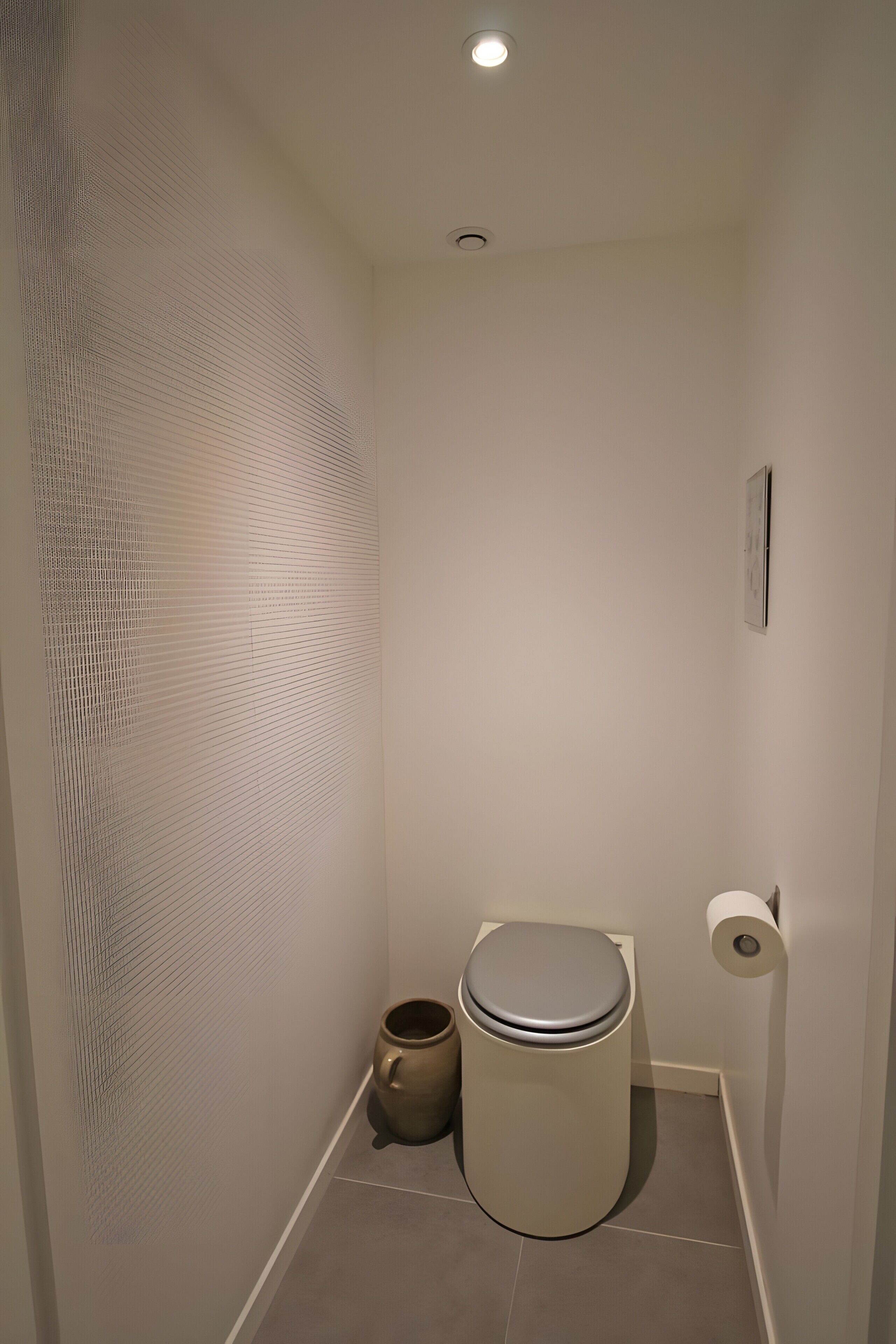 Une petite salle de bain propre, équipée de toilettes, d’une poubelle et d’un porte-rouleau de papier toilette.
