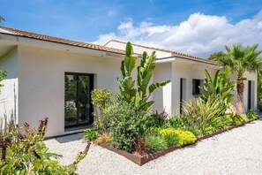 Ein modernes Haus mit heller Fassade, großen Fenstern und einer Auffahrt mit Kies.