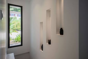Ein Flur mit einem großen Fenster, weißen Wänden und drei schwarzen Vasen auf Regalen.