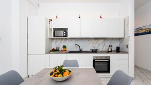 A modern kitchen with white cabinets, a microwave, a sink, and a stove. There is a bowl of fruit on the table. - YourHome - Maremi Apartment (Piano di Sorrento)