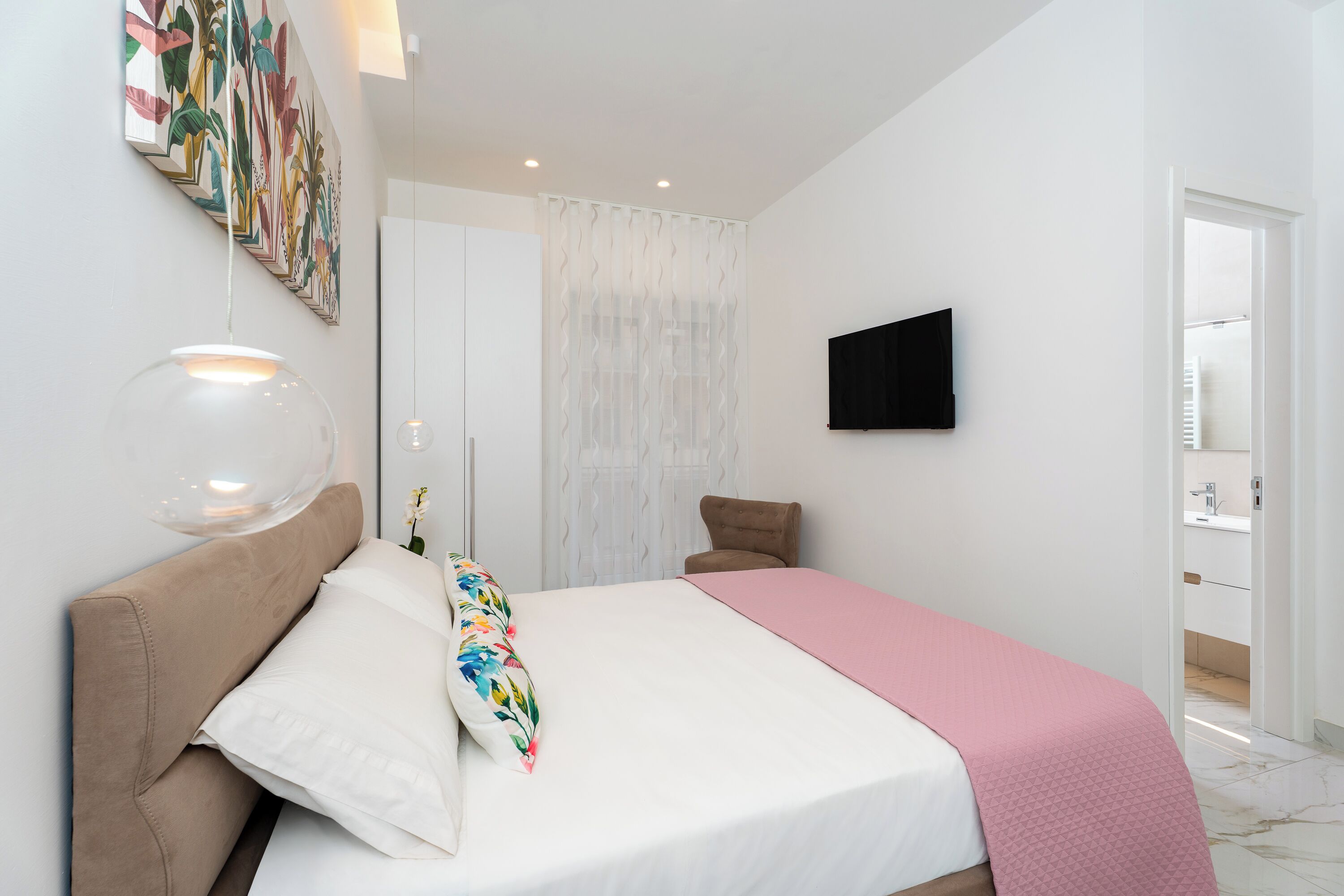 A modern bedroom with a large bed, a wall-mounted TV, and a decorative wall piece.