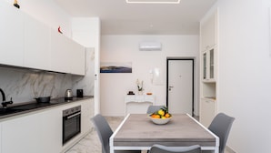 A modern kitchen with white cabinets, a marble countertop, and a dining area with a table and chairs. - YourHome - Maremi Apartment (Piano di Sorrento)