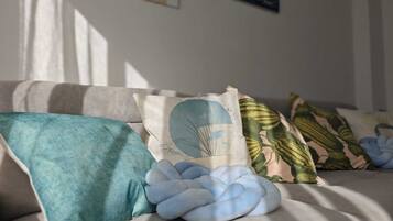Un sofá con varios cojines, incluyendo uno con forma de nube azul, en una habitación con luz solar entrando por la ventana.