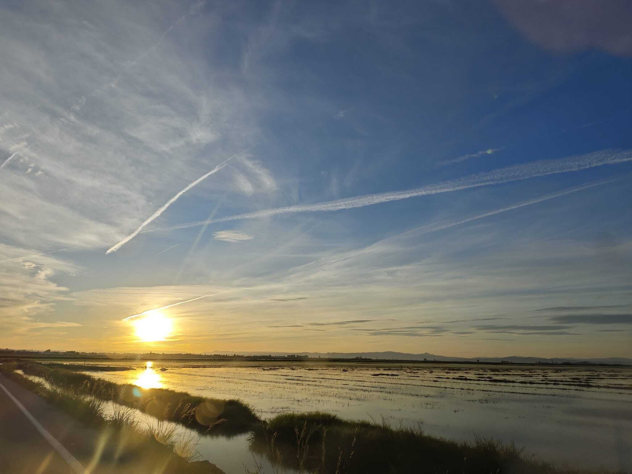 Atardecer sobre un paisaje llano con agua y montañas al fondo.