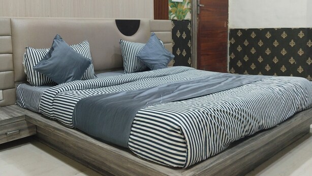 A bedroom with a bed, pillows, a wardrobe, and a wall with a leaf pattern. - HOTEL DYNA INN (Gwalior)