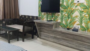 A living room with a sofa, a dining table, and a TV mounted on a wall with a leaf pattern. - HOTEL DYNA INN (Gwalior)